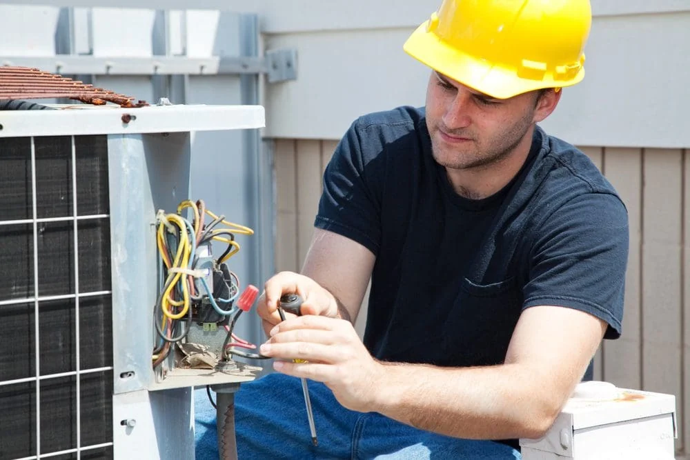 Technician carefully repairing electrical components inside an outdoor HVAC unit